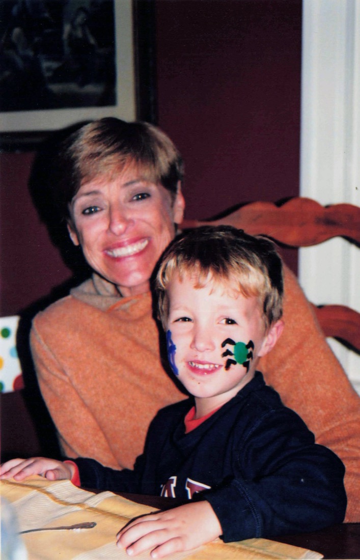 Jake as a young boy with face paint, smiling at the dinner table on his grandmother Nana's lap. She is smiling in an orange sweater.
